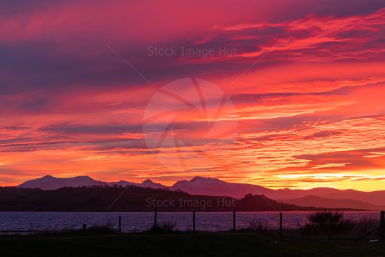 Sun turns sky red as sun sets behind the mountains of Arran, Scotland