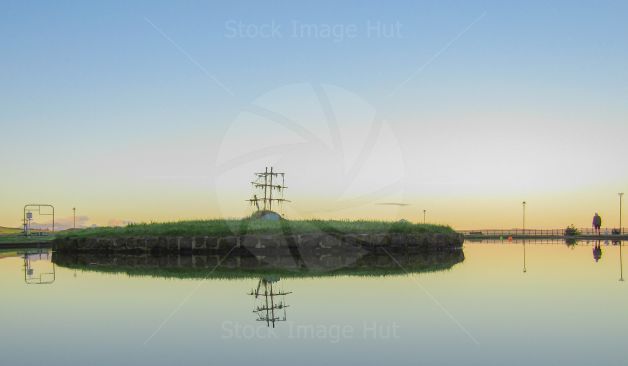 An old model boat sitting on a small island in the middle of boating pond on a beautiful calm morning