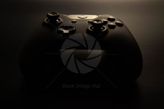 Very dark, low light shot of a single Xbox black controller with a small light hitting the \'X\' button image