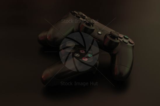 Two Playstation controllers sitting on matt black surface in low light image