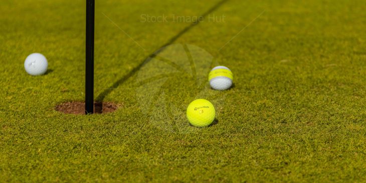 Golf Balls sitting next to pin on golf green