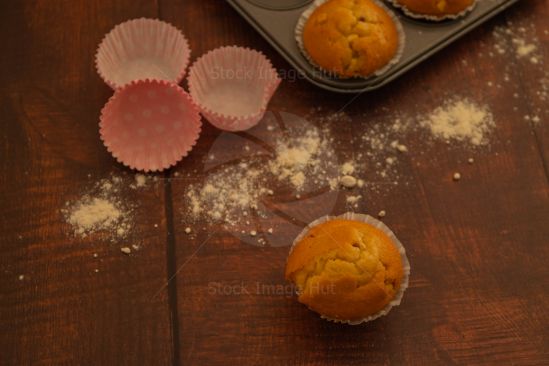 Freshly baked muffins sitting on wooden board with empty cup cake cases