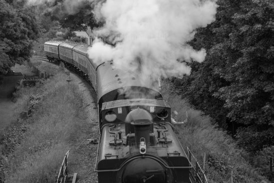 Steam train from overhead bridge in black and white image