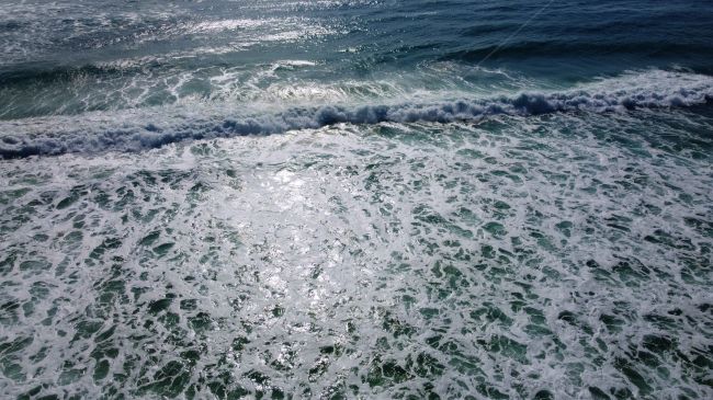Waves going out as sun shines on them, taken from a drone image